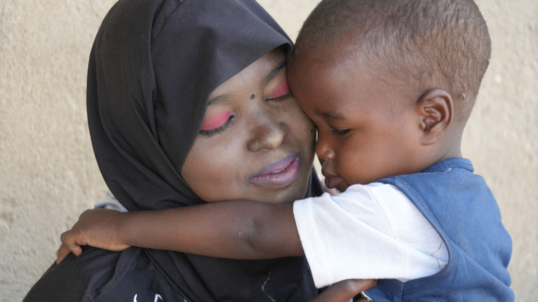 Close-up shot of a boy and his mother hugging, their faces resting on each other.