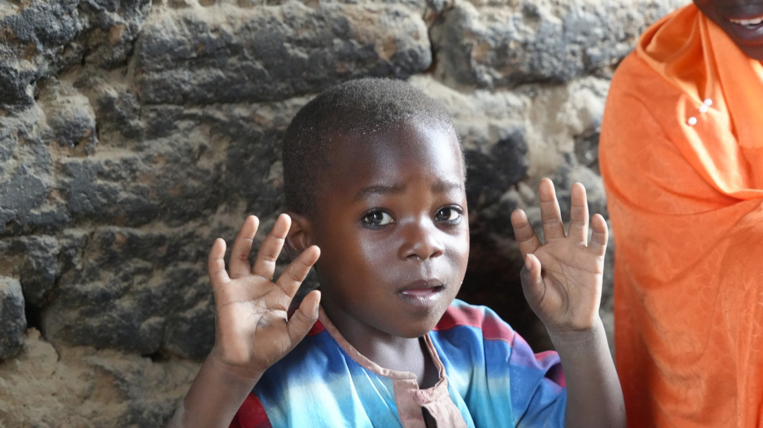 Yacouba looks at the camera and raises both hands in the air, palms open and fingers outstretched.