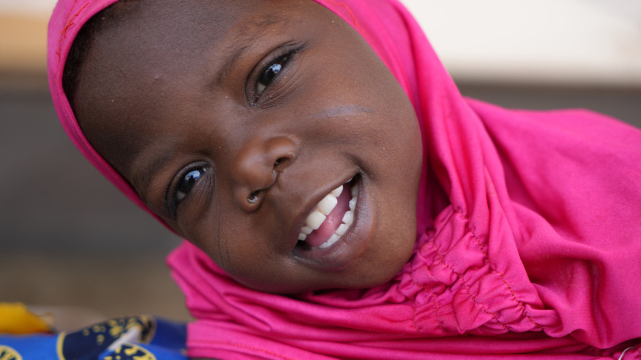 Portrait of Massalouka, a young girl wearing a pink head covering, smiling at the camera