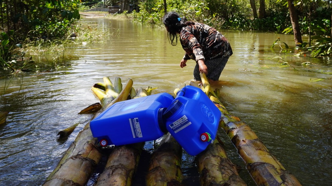 A woman has to cross flooded fields to reach her house with water jerry cans and hygiene kits supplied by HI as part of its emergency response. 500 households affected by the floods have already received support from HI in the province of Davao del Norte