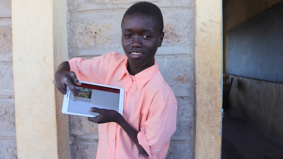 Patrick, smiling, shows the story on a tablet he just read in a digital class