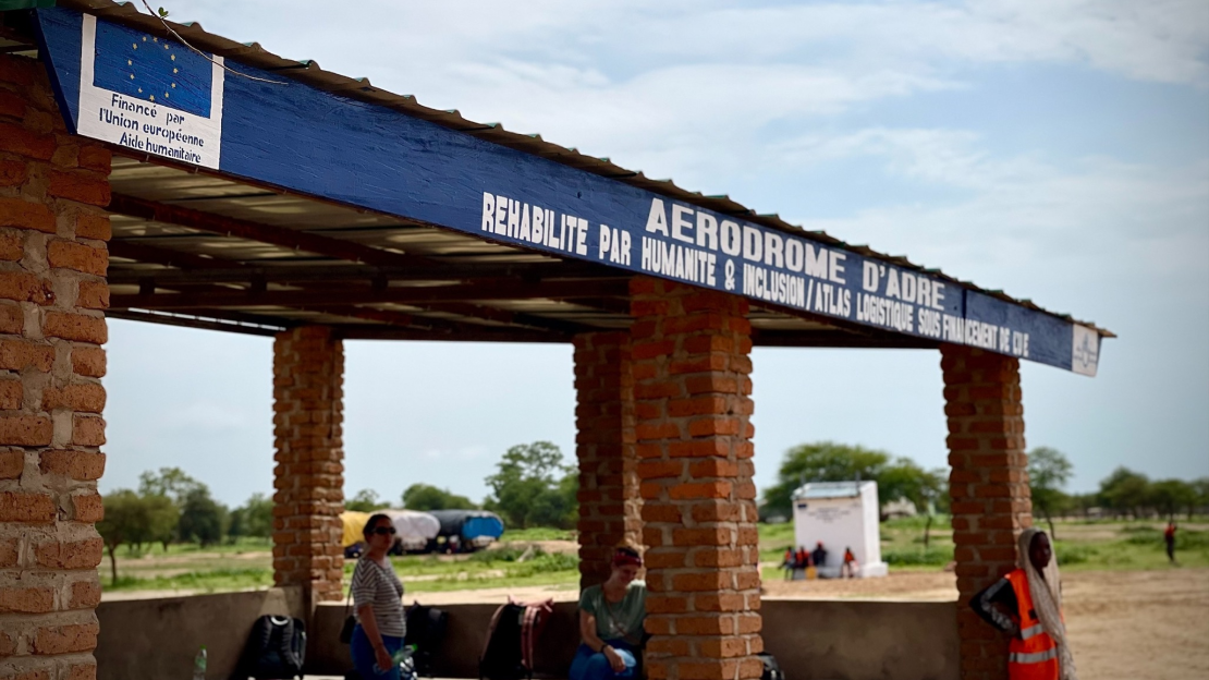 Several people stand under the awning at the entrance to the rehabilitated airfield.