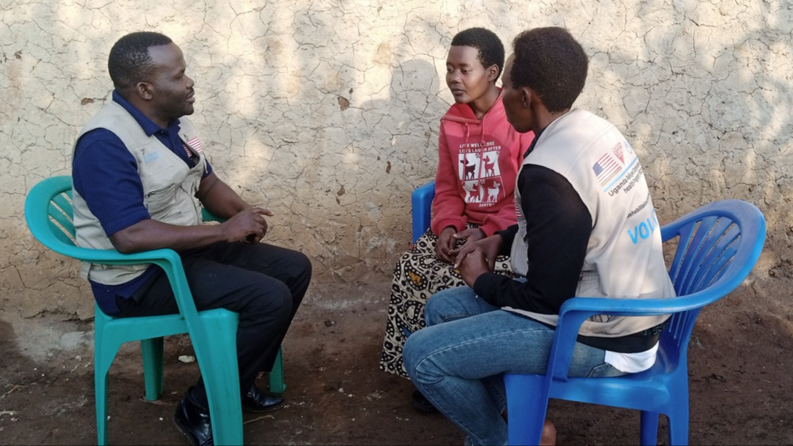 Three people, two women and a man, are sitting in a circle on plastic chairs, talking.