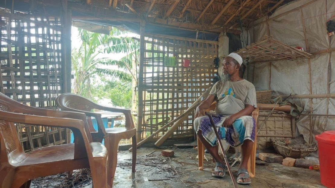 A man wearing a white bucket hat sits in a chair with a cane in his hand while staring off into the opposite directions.