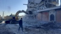 Man walking in front of destroyed building's rubble and an excavator