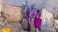 Amina (center), stands with her husband (left) and one of her three children (right) in front of their new home in a Hargeisa displacement camp. 2022. © HI
