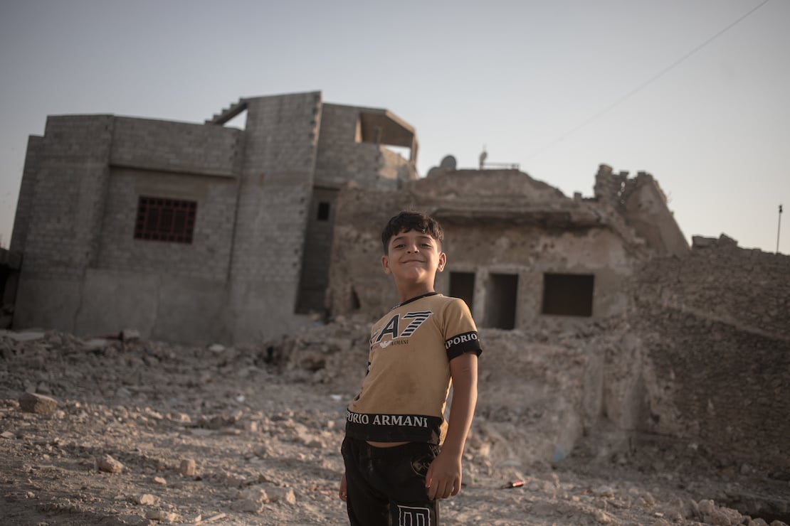 A chld stands in front of a ruined building, Mosul, Iraq