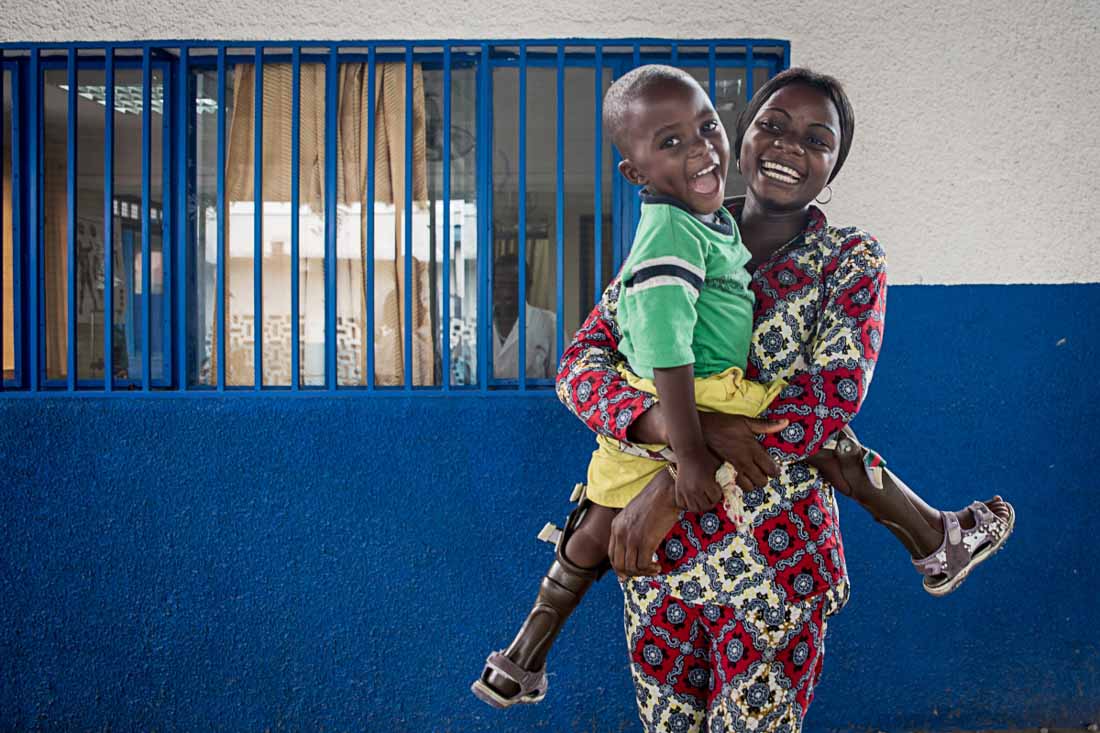 A young boy being held by his mother and smiling in Mama Yemo General Hospital, DR Congo.