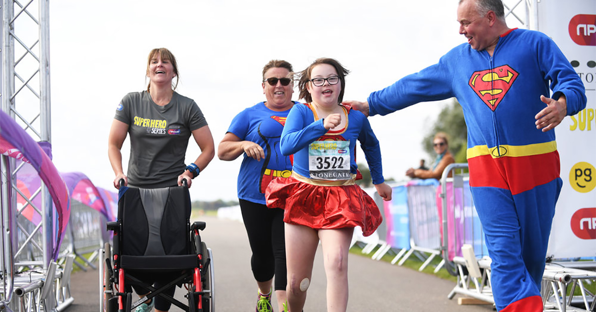 A family crossing the finish line in superhero outfits