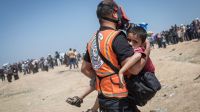 A medic carrying a child to an ambulance after inhaling tear gas, on 14th May 2018 in Gaza City. 