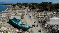 People drive past a washed up boat and collapsed buildings in Palu on 1st October 2018, after an earthquake and tsunami hit the area.