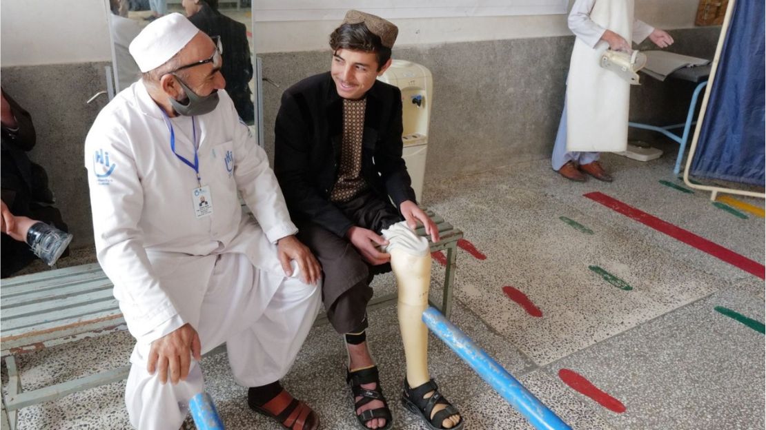 Young boy smiling with prosthetic leg next to Humanity & Inclusion rehabilitation specialist