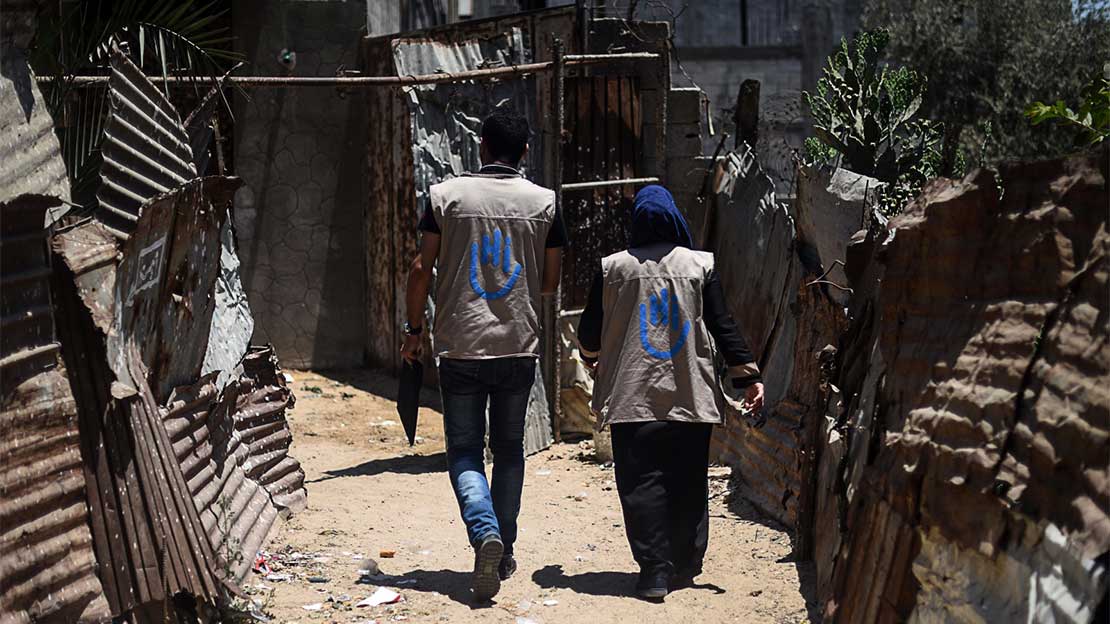 Two members of HI's emergency mobile team walk down a dirt road after conflict in Gaza in 2018.