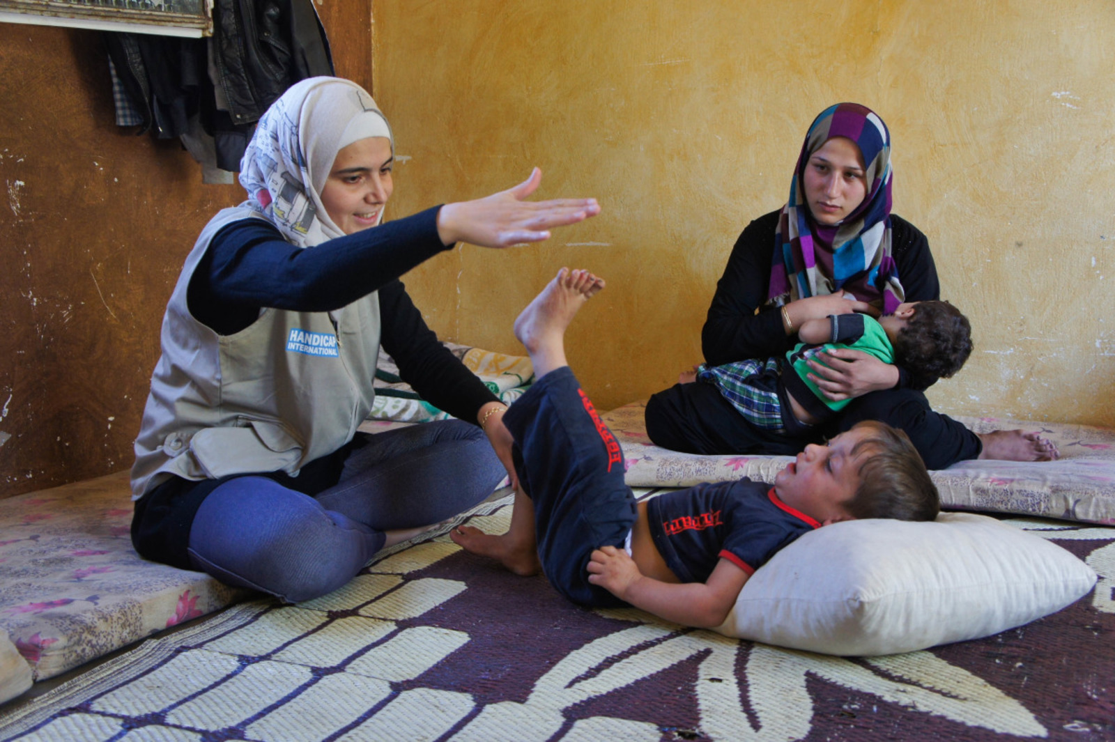 Fayez lies on his back and lifts his leg to touch Mariam's hand as part of his rehabilitation exercises.