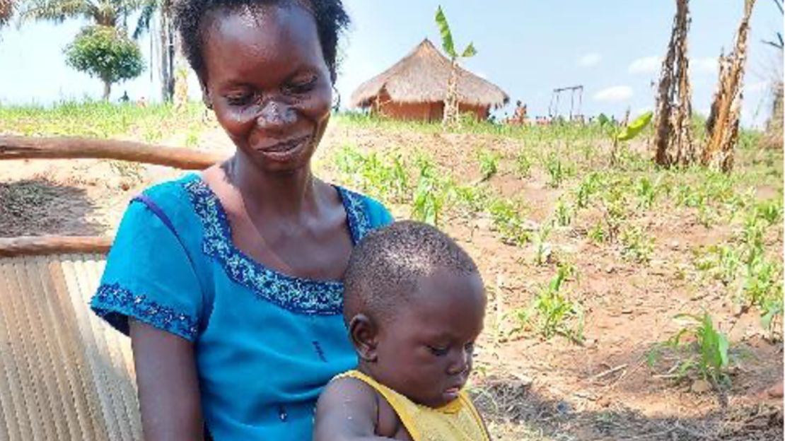 A Black woman wearing a blue shirt smiles while holding her small son.