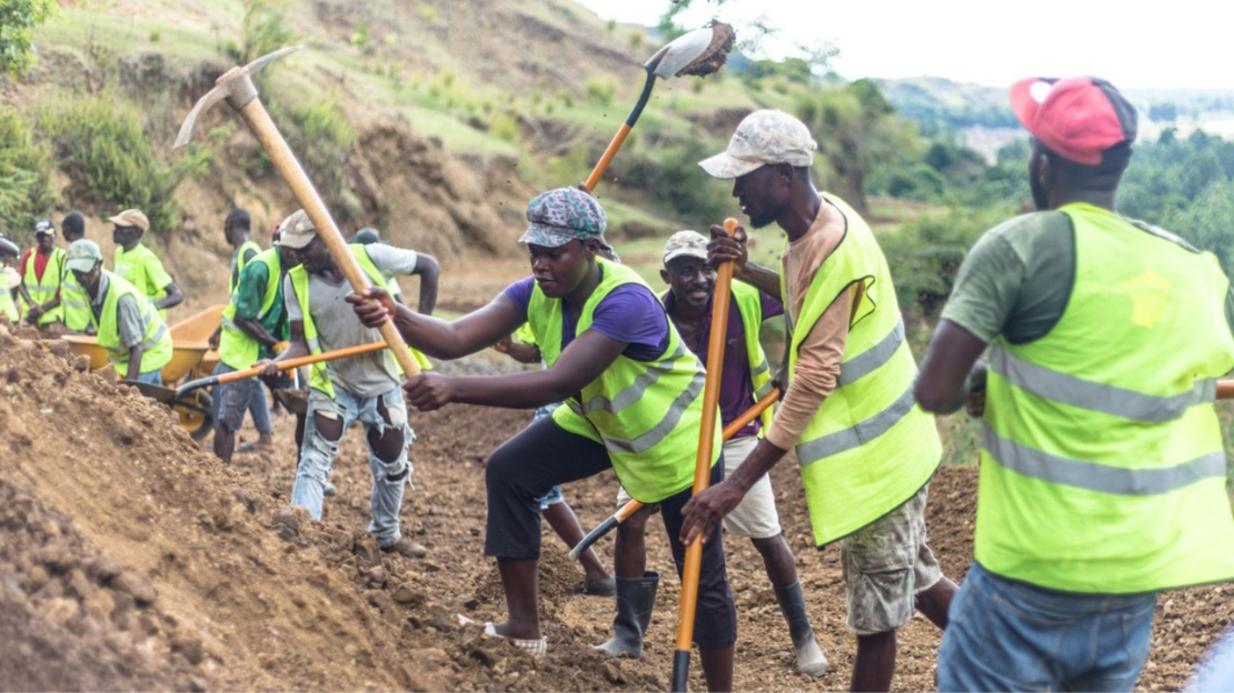 10 people wearing neon green vests using pix axes to dig into the side of a hill