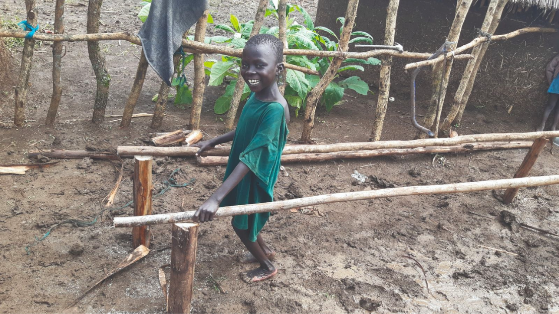 Young boy smiling as he stands outside between two parallel bars made of wood.