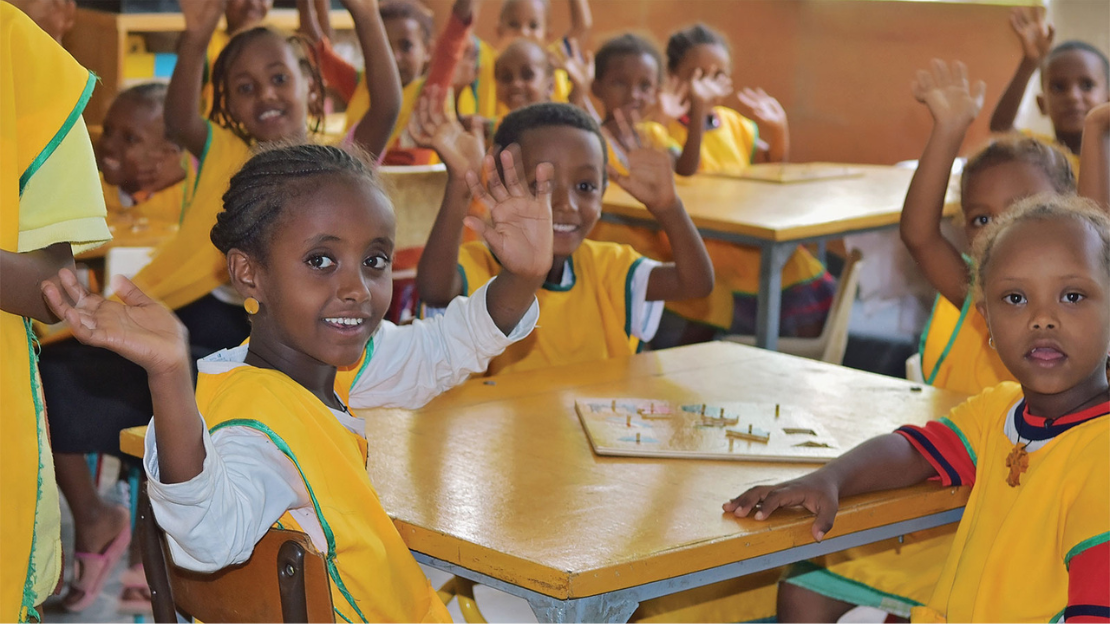 Classroom full of smiling and waving children, all wearing yellow school uniform