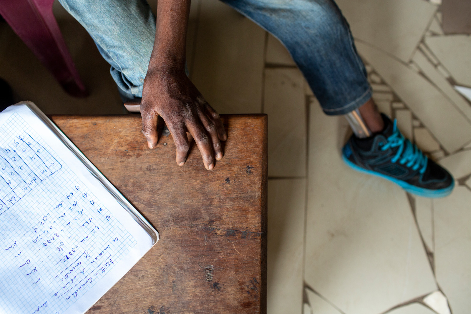 Tresor, a young boy from DRC is writing his school work at a table. Image taken from a birdseye view. 