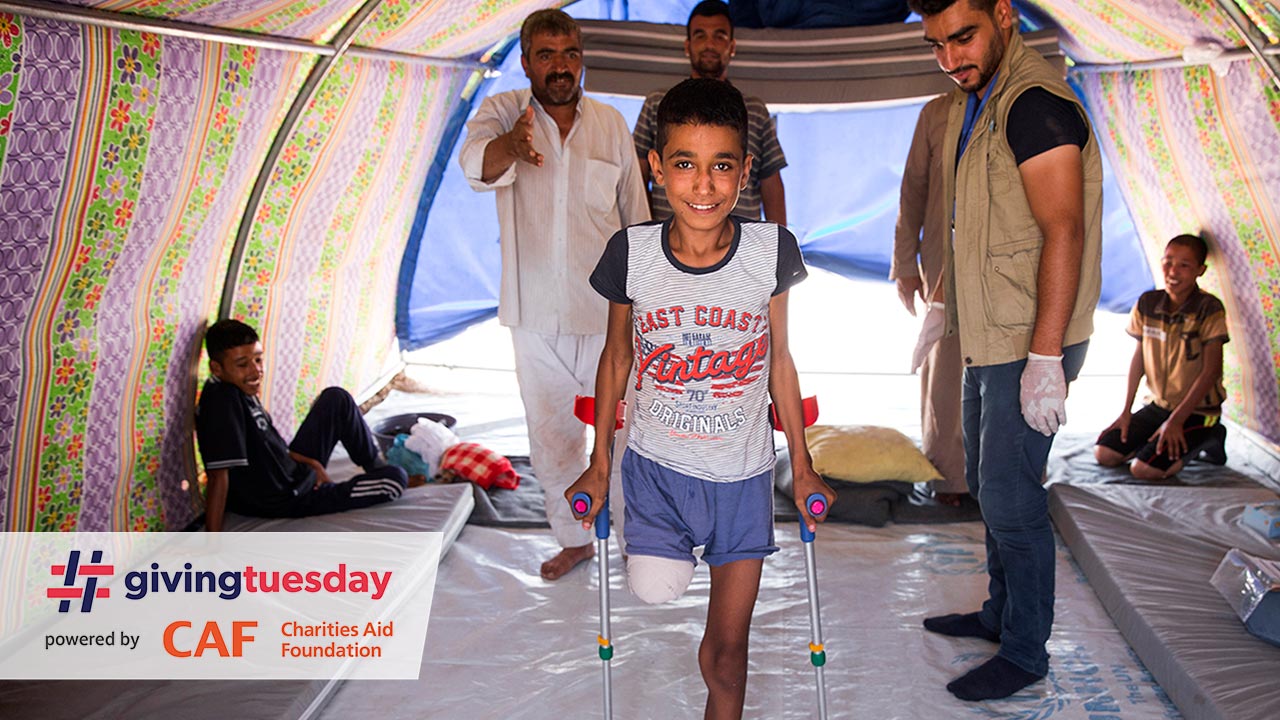  Abdel Rahman stands with crutches in his tent, while HI physical therapist Mohammed looks on.