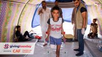  Abdel Rahman stands with crutches in his tent, while HI physical therapist Mohammed looks on.