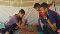 Abdallah and his older brother play drafts in their tent.