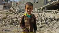 A child stands in front of damaged buildings in Jalawla, Iraq.