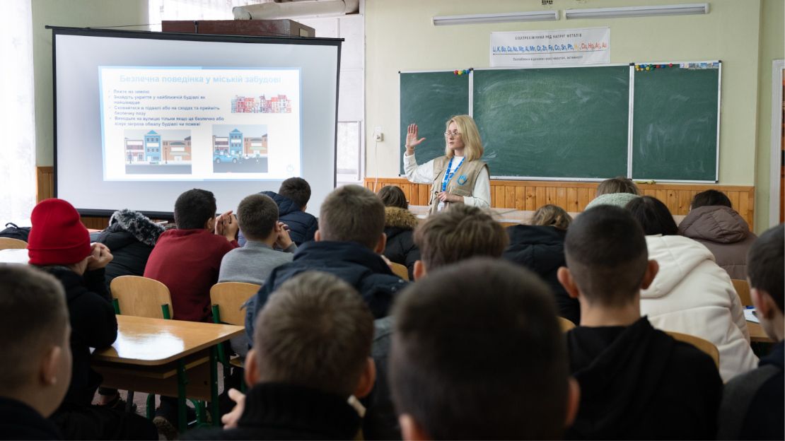 A woman stands in front of a classroom of children.